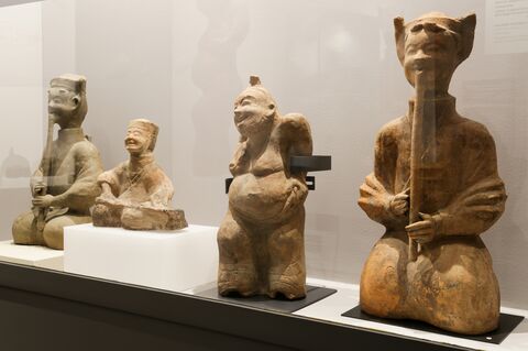 Four seated Han-dynasty ceramic figures displayed together, including musicians holding long instruments.