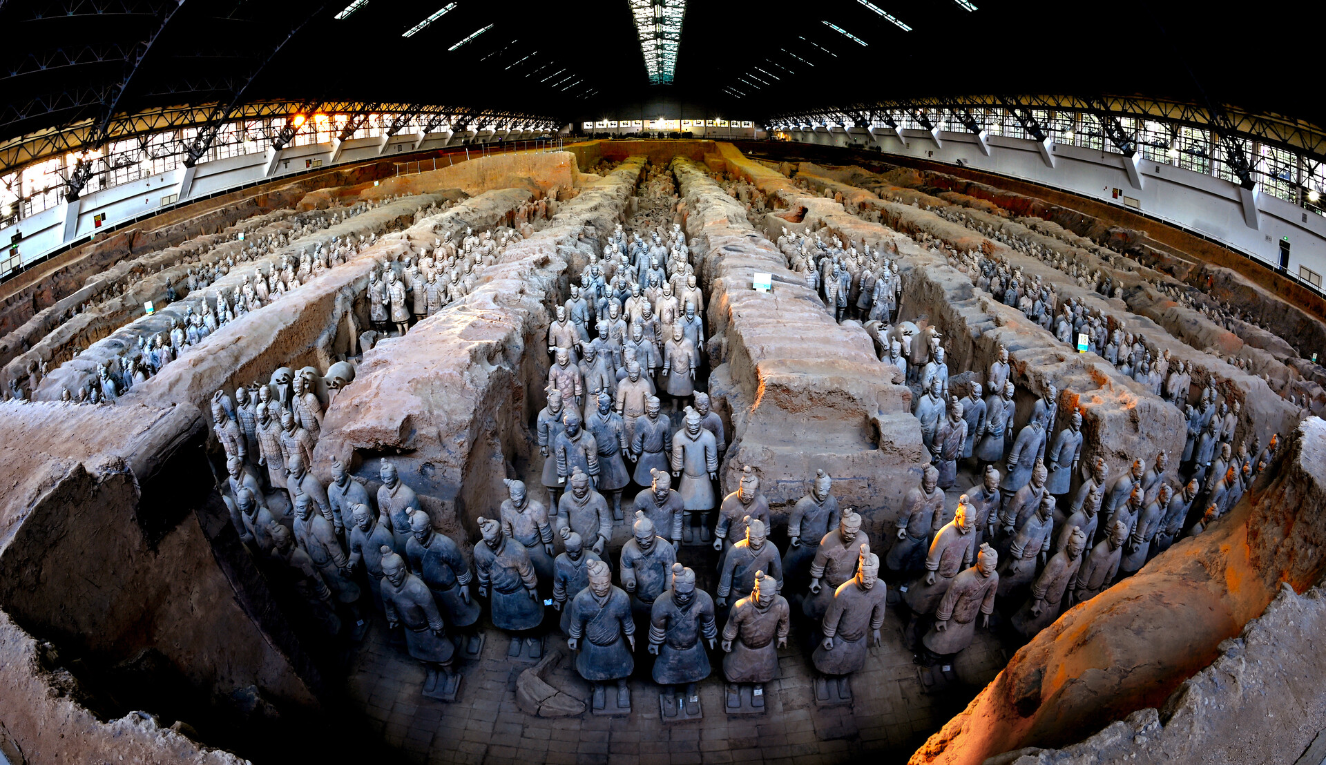 Panoramic view of rows of terracotta warriors in Pit 1, separated by earthen partitions beneath a steel-roofed hall.