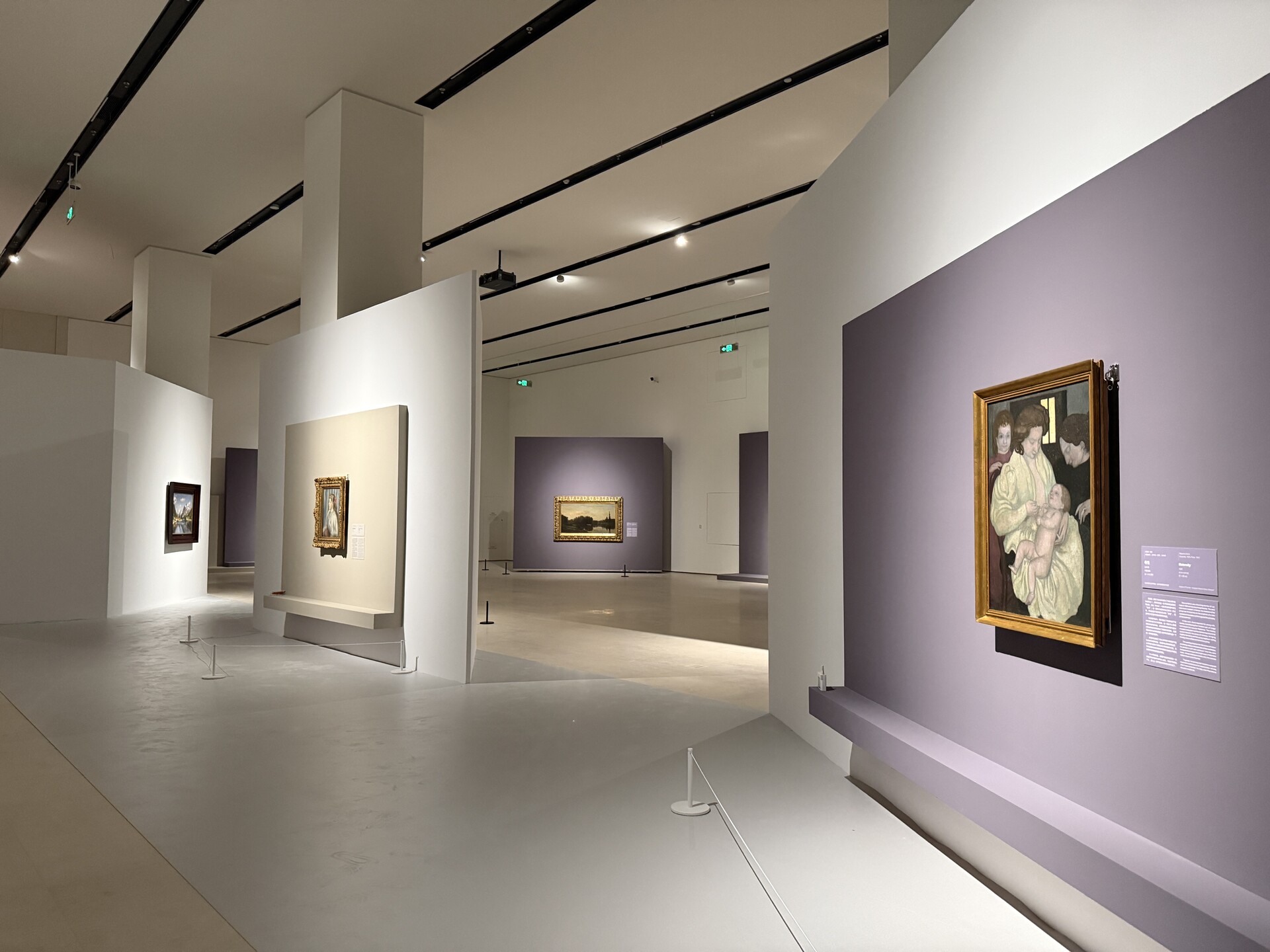 “大师之境”在深圳国际美术博物馆的展厅现场，欧洲绘画作品以金色画框陈列在紫色和白色展墙上，顶部设有轨道灯。