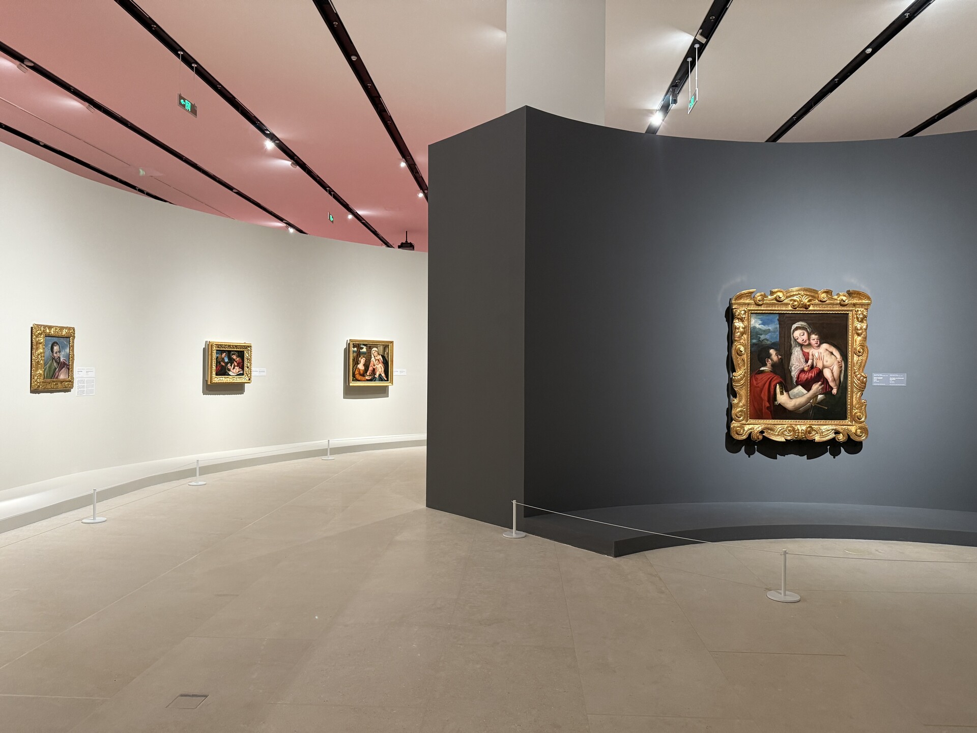 《大师之境》展览现场：多幅欧洲绘画装裱于金色画框中，陈列在浅色与深色弧形展墙上方，深圳国际美术博物馆展厅顶部为粉色调灯光。